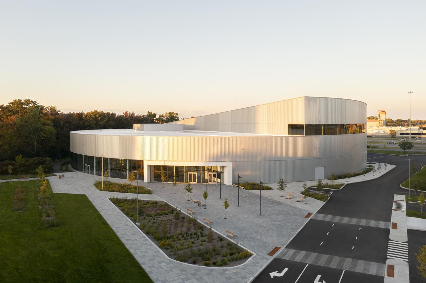 Vue extérieure du Complexe aquatique de Laval, bâtiment moderne en forme circulaire avec revêtement métallique, entouré d’un aménagement paysager soigné et de larges sentiers pavés.