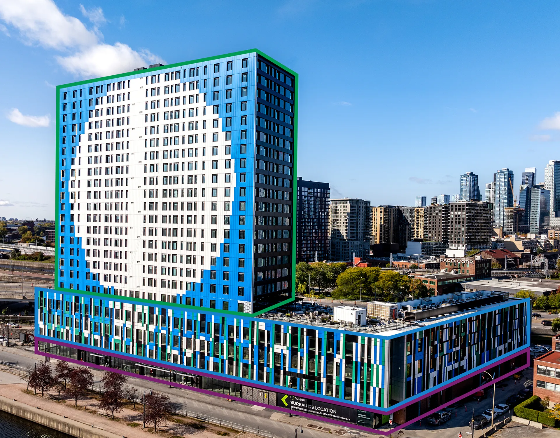 Vue extérieure du bâtiment Haleco à Montréal, un immeuble résidentiel coloré à l’architecture contemporaine, situé en bordure du canal de Lachine, avec les tours du centre-ville en arrière-plan.
